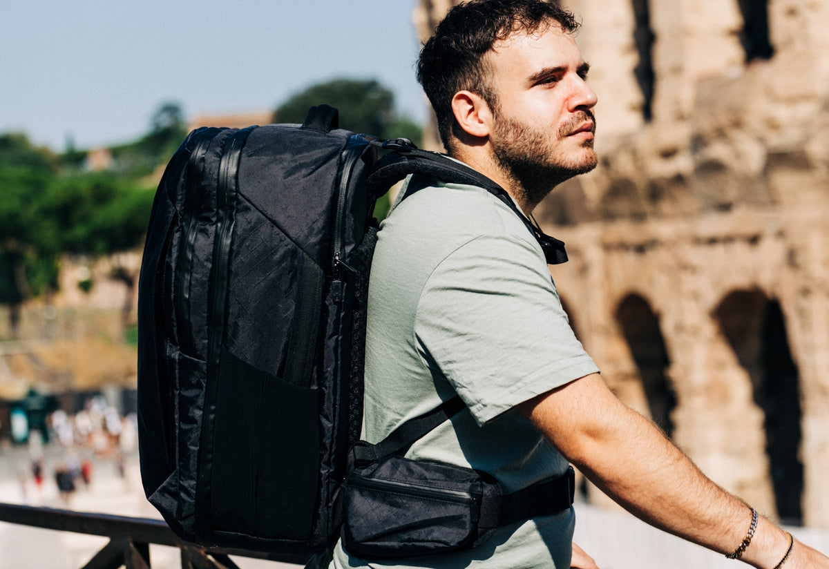 Two travelers carrying Tortuga backpacks through a city square
